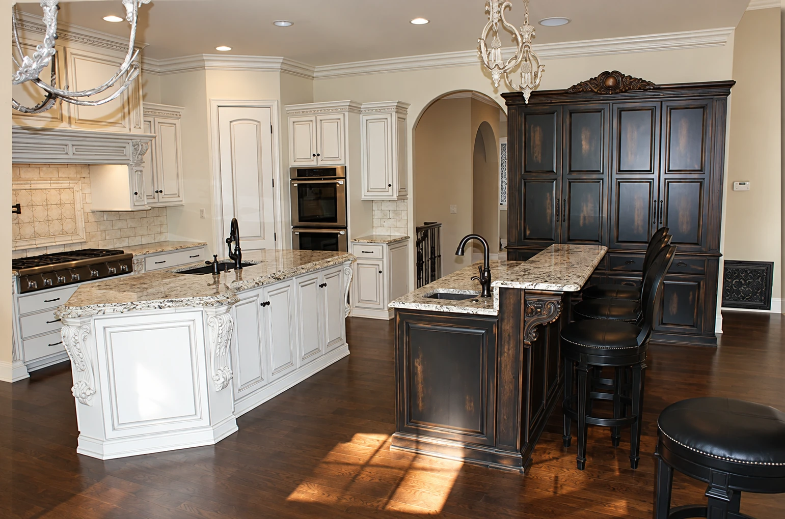 Light perimeter cabinetry meets a deep-toned island and tall cabinet in a contrasting kitchen composition.
