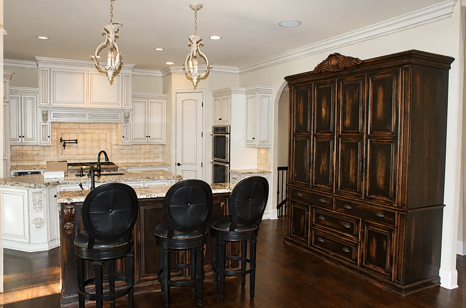 Light perimeter cabinetry meets a deep-toned island and tall cabinet in a contrasting kitchen composition.